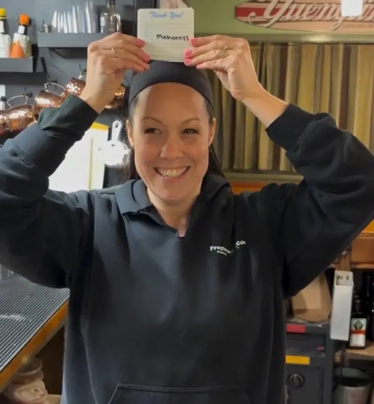 A Frogtown server holding up a handwritten thank-you card from a regular